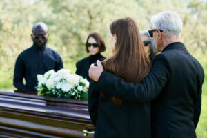 Família enlutada durante cerimônia de despedida, observando o caixão adornado com flores brancas, momento que antecede o translado funerário.